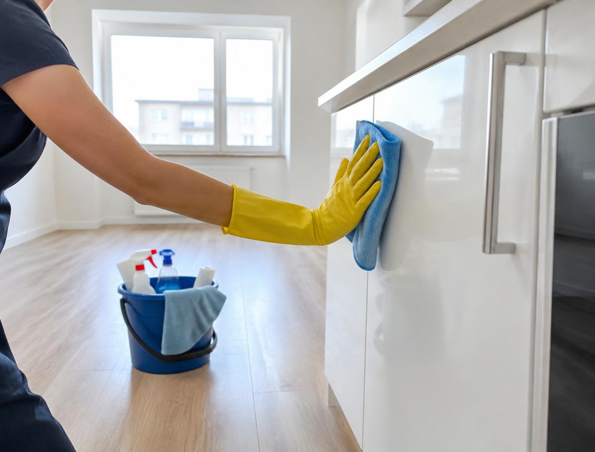 Gloved hand wiping a white cabinet in an empty clean apartment